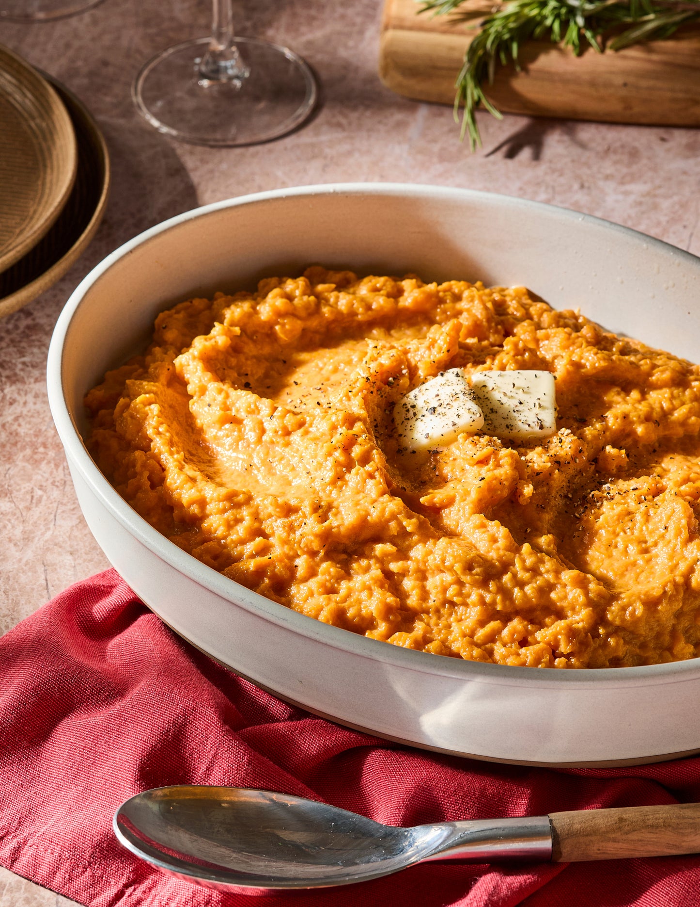 Bowl of creamy sweet potato mash with butter on a red cloth.