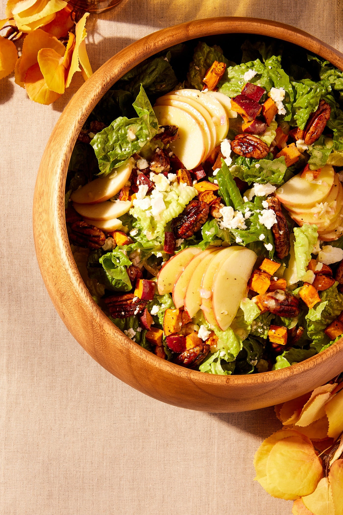Brown wooden bowl filled with lettuce with apples, pecans, and squash on top along with salad dressing.