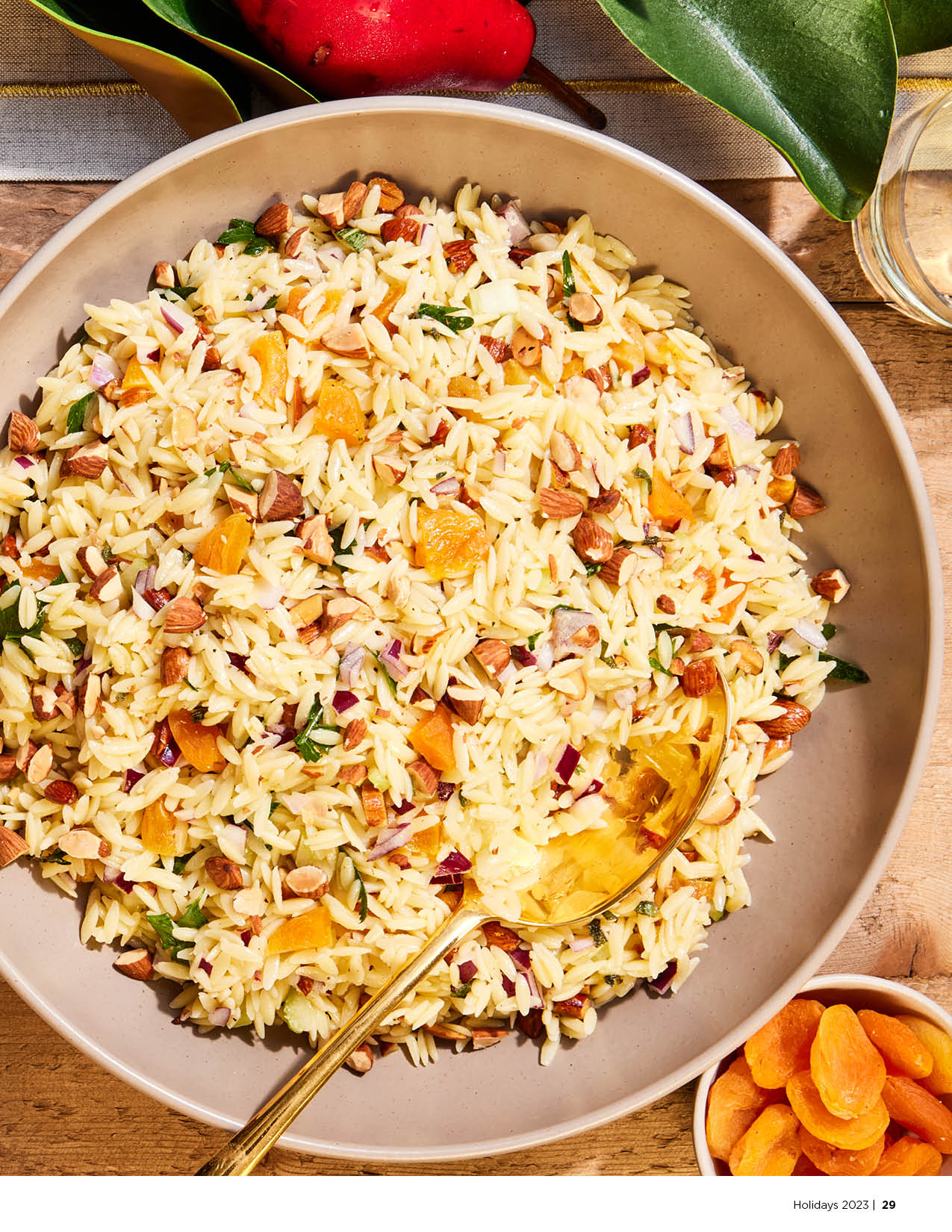 Orzo salad with dried apricots and almonds sitting on a wooden table in a brown bowl.