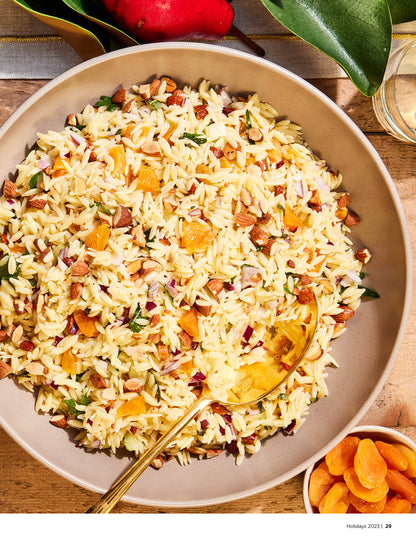 Orzo salad with dried apricots and almonds sitting on a wooden table in a brown bowl.