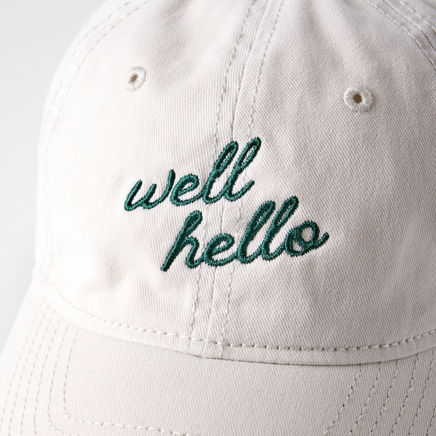 White cap with 'well hello' embroidery on a light gray background