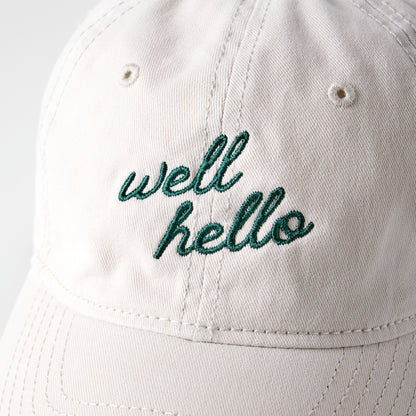 White cap with 'well hello' embroidery on a light gray background