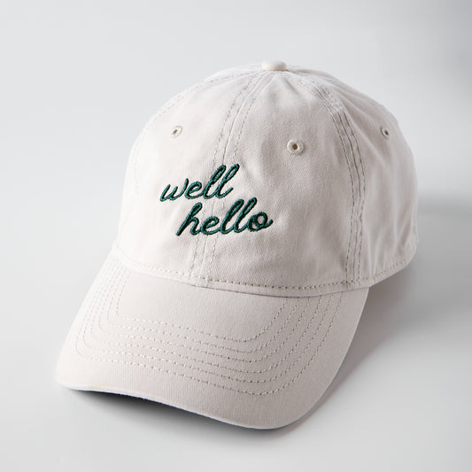 Beige cap with 'well hello' embroidery on a light gray background